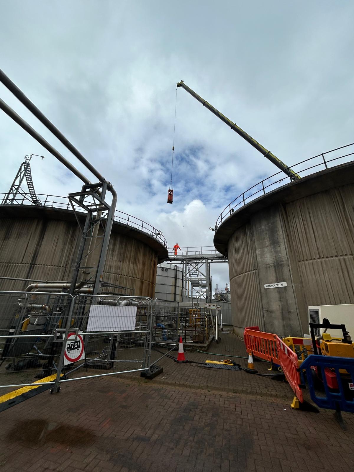 Mobile crane lifting equipment between concrete gas holder tanks on live site
